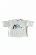 White cropped tee with blue ombre ABC chenille letter appliqué flat lay on white background