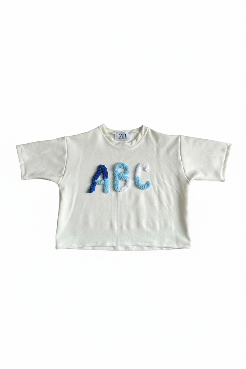 White cropped tee with blue ombre ABC chenille letter appliqué flat lay on white background