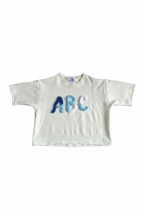 White cropped tee with blue ombre ABC chenille letter appliqué flat lay on white background