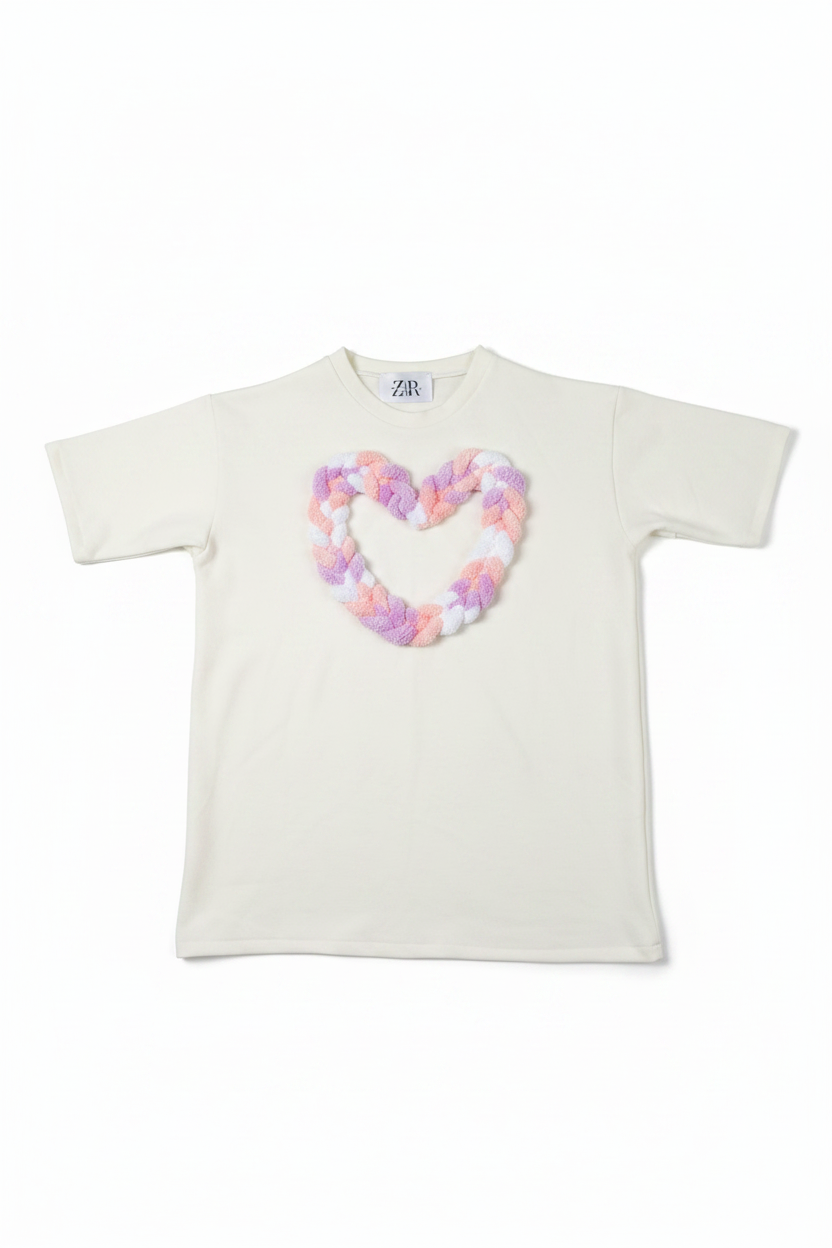 White oversized tee with pastel braided heart appliqué flat lay on white background