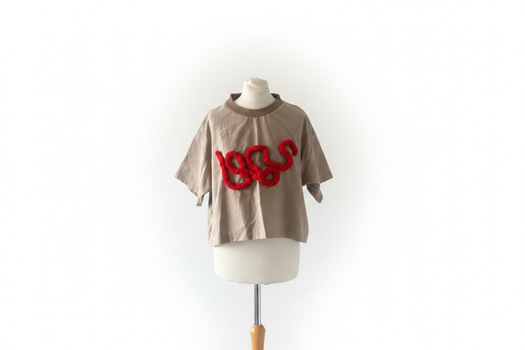 Beige cropped t-shirt with red yarn squiggle appliqué on mannequin with white background